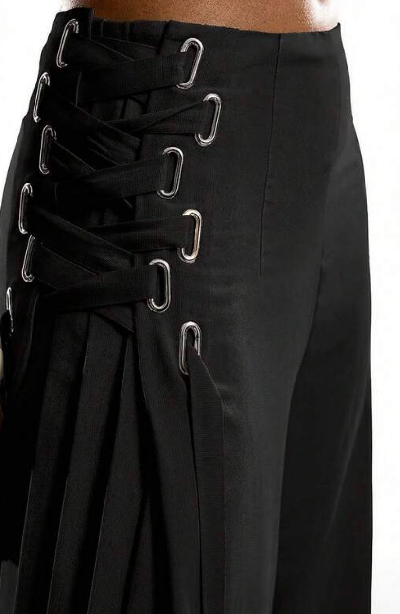 Close-up of a black skirt with multiple side laces and silver metal eyelets, shown on a model against a white background.